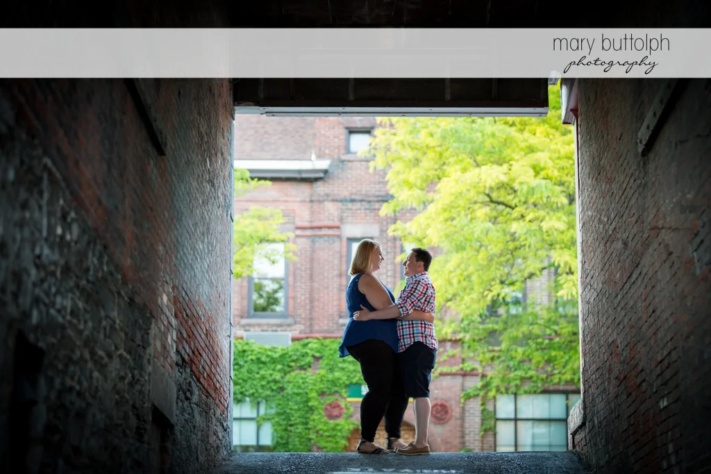 Couple stand between brick walls at Skaneateles Lake Engagement