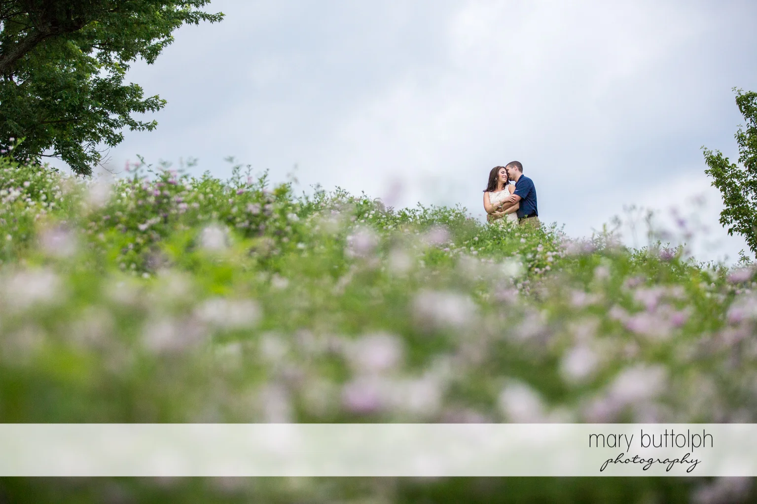 Couple embrace in the garden full of flowers at Skaneateles Engagement
