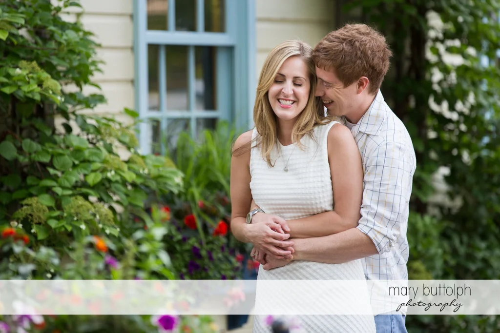 Couple embrace in front of a house at Skaneateles Engagement