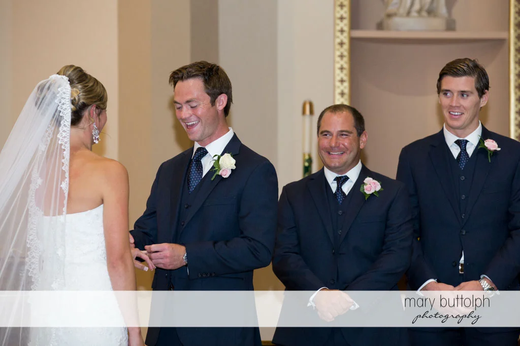 Groom slips the ring on the bride's finger as the groomsmen look on at Skaneateles Country Club Wedding