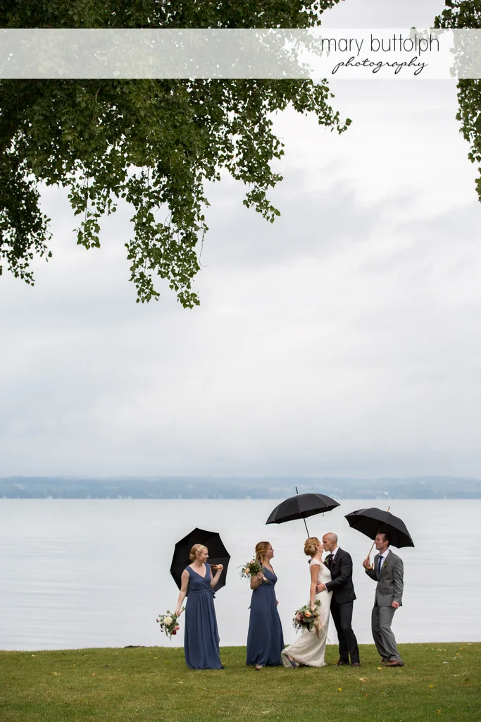 The wedding party with umbrellas pose near the lake at the Inns of Aurora Wedding