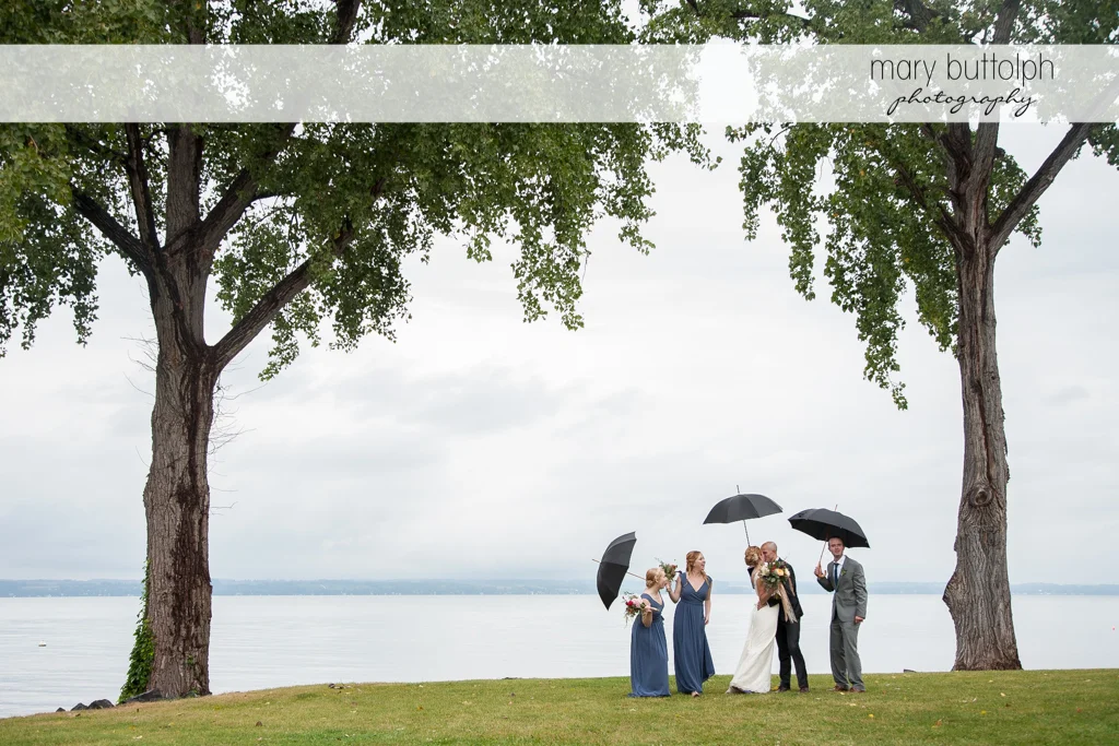 Long shot of the wedding party with umbrellas by the lake at the Inns of Aurora Wedding