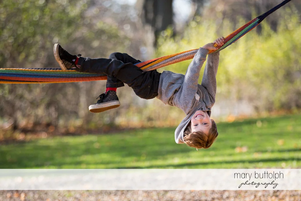 Boy hangs from a hammock in the backyard at Skaneateles