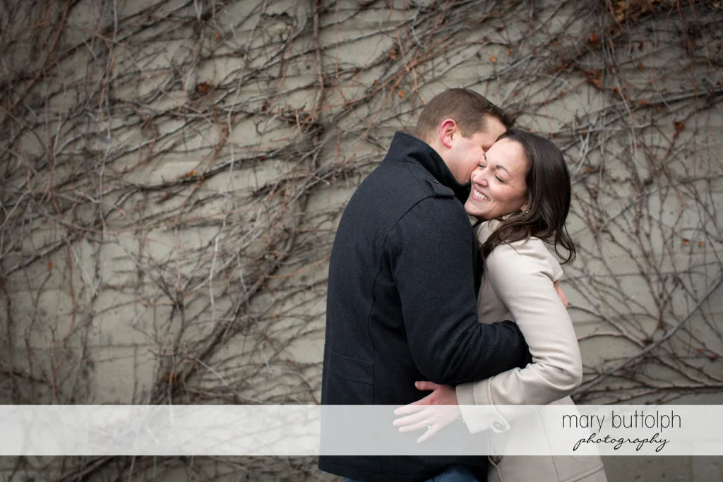Couple embrace in front of a wall at Skaneateles Engagement