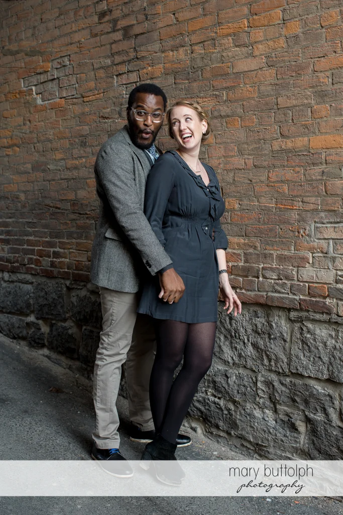 Couple clown around in front of a brick wall at Skaneateles Engagement