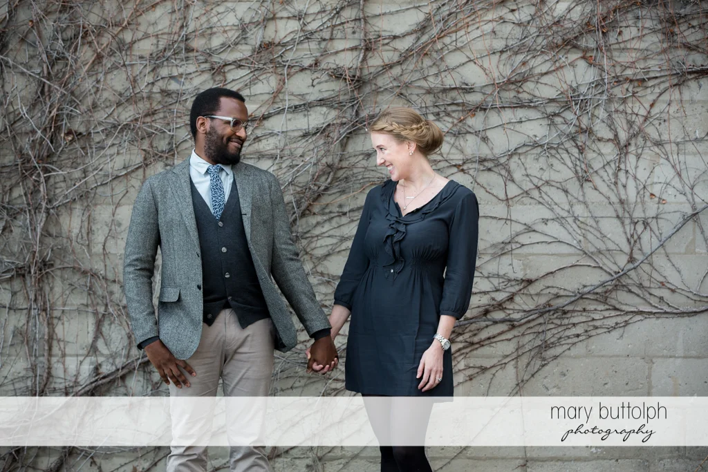 Couple hold hands in front of stone wall at Skaneateles Engagement