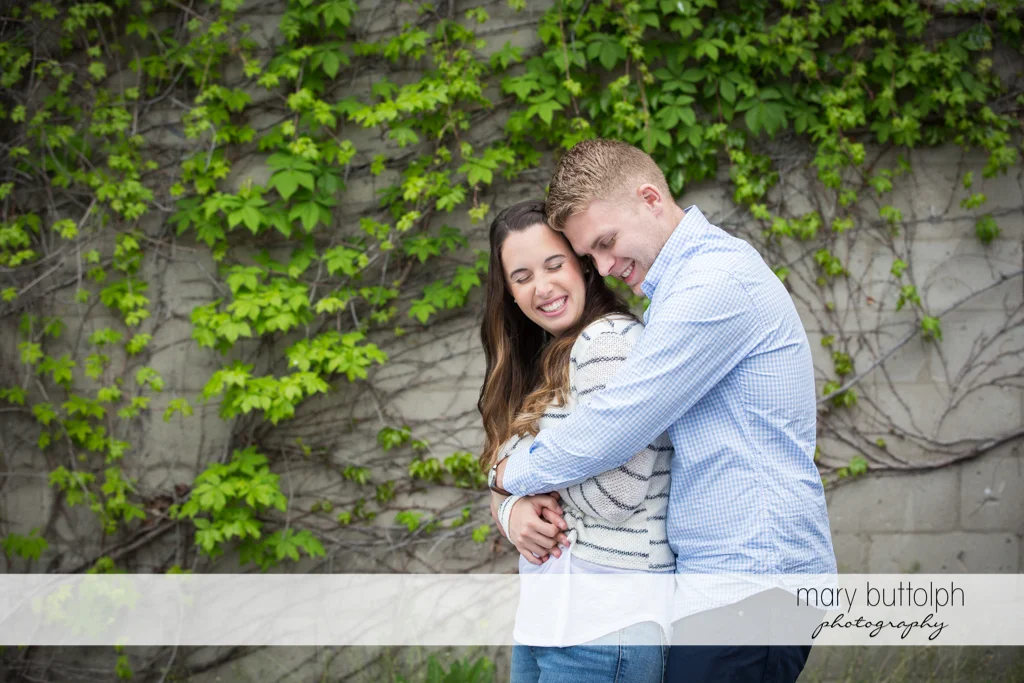 Couple embrace in front of a wall at Hobbit Hollow Engagement