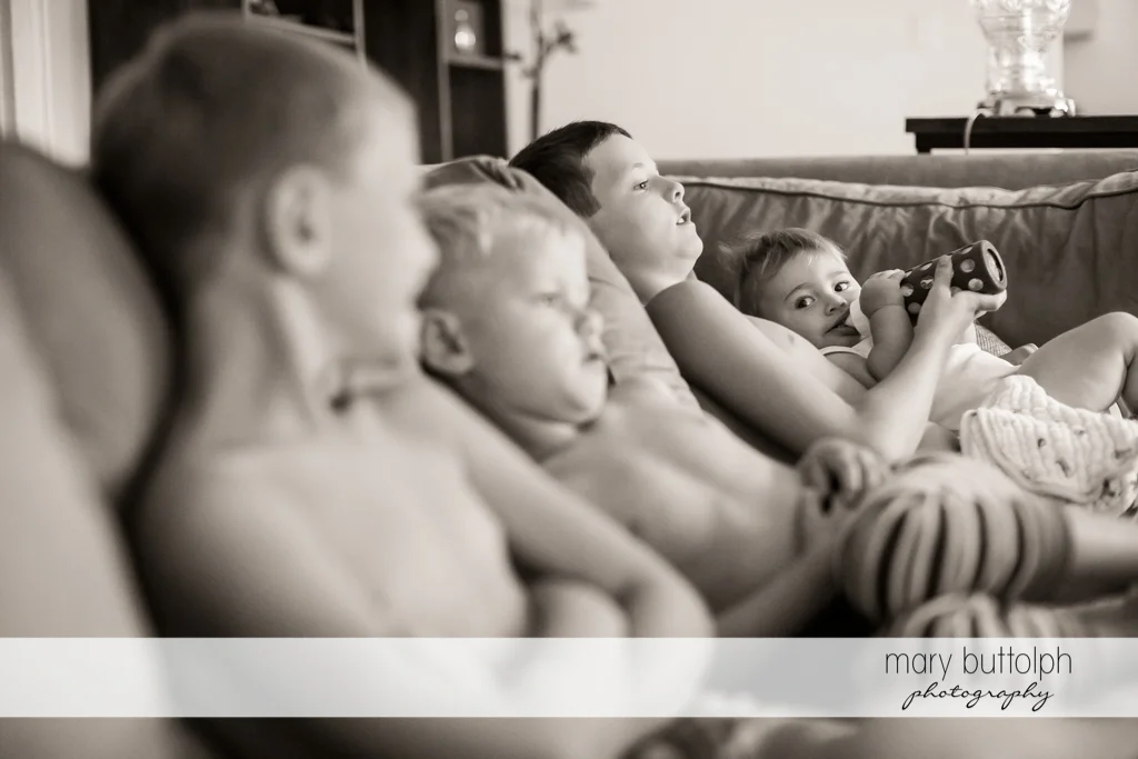 Siblings sit on the couch while their younger sister drinks milk at Skaneateles