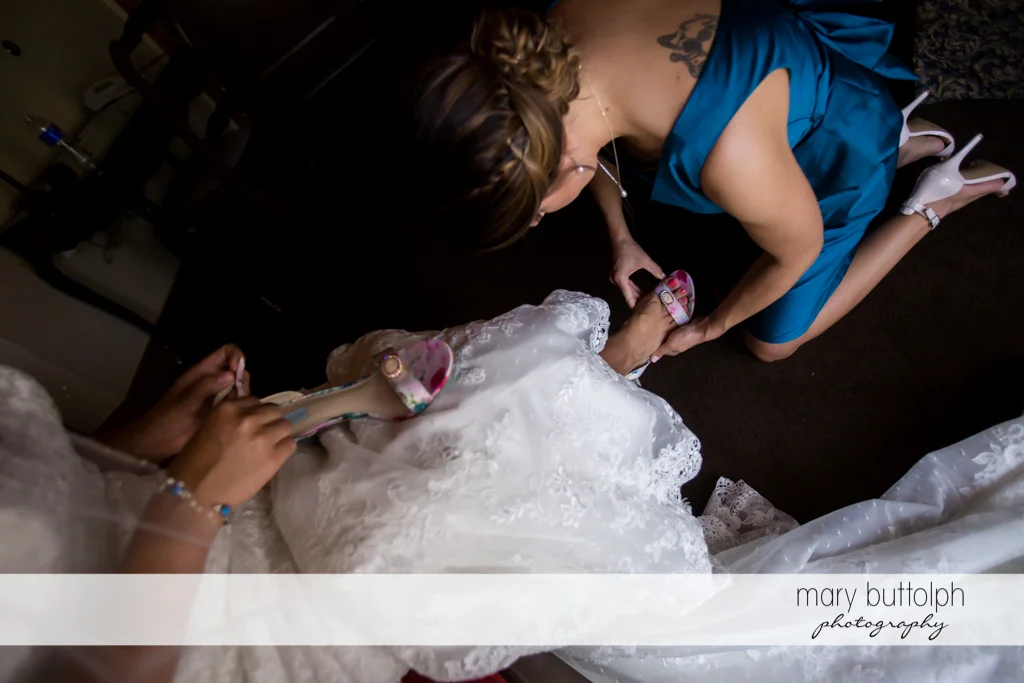 Woman helps put on the bride's shoes at The Lodge at Welch Allyn Wedding