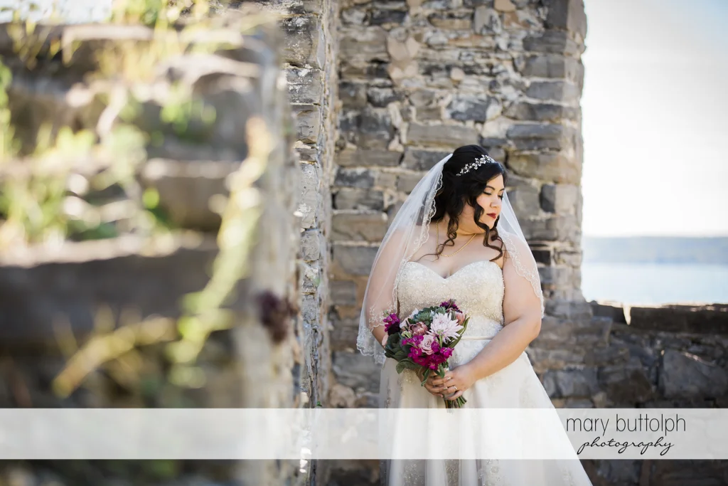 Bride poses with flowers in front of a brick wall at Aurora Inn Wedding