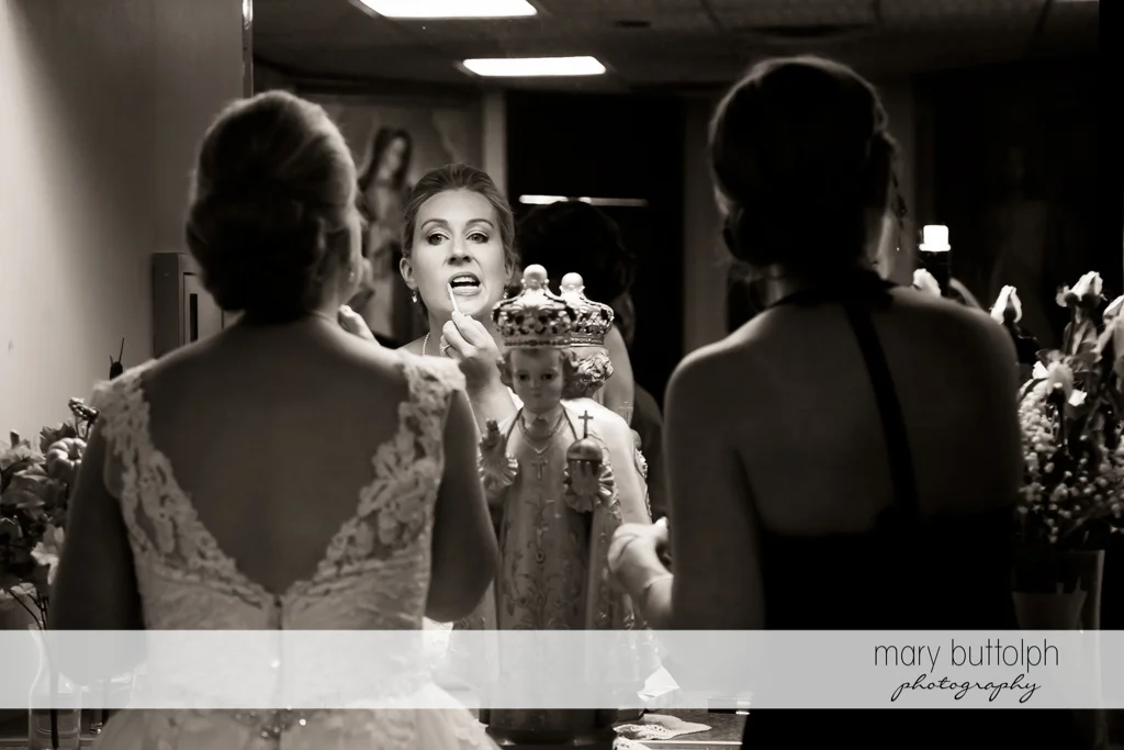 Bride applies lip gloss in front of a small statue of the Baby Jesus at SKY Armory Wedding