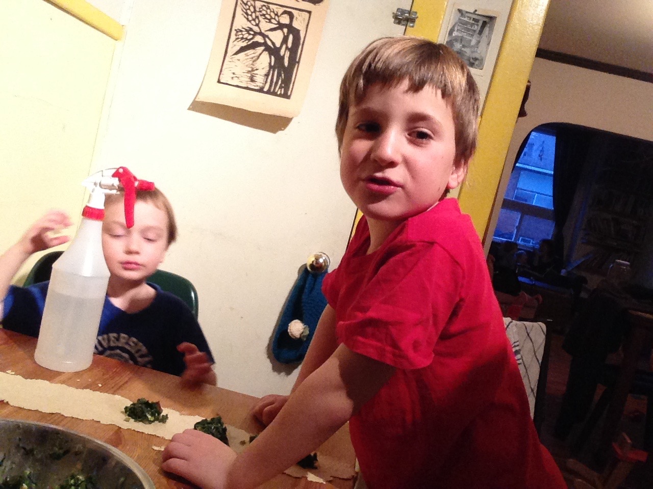Children ages 4.5 and 6.5 work on spinach and feta cheese. Spray bottle in both shots is for sticking the sheets of pasta together. 