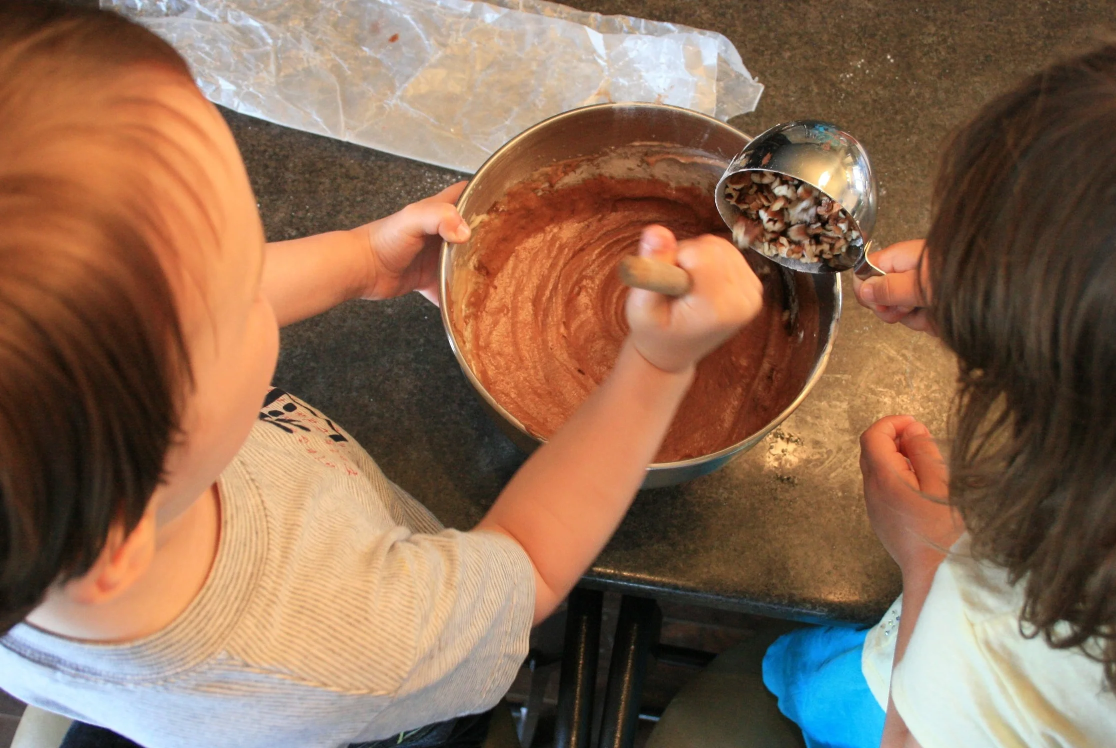 Five-year-old cousins working together: adding pecans to the brownie batter.