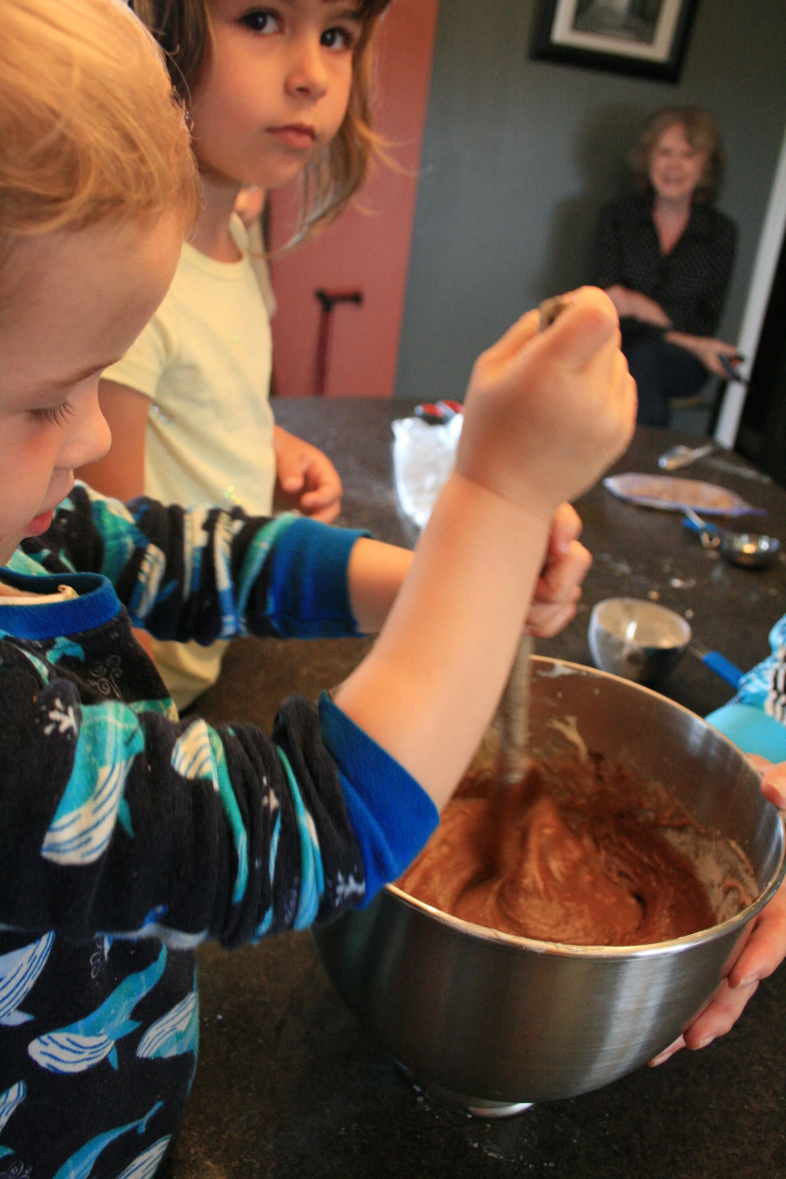 Three-year-old mixes brownie batter, 5-year-old and Grandma look on