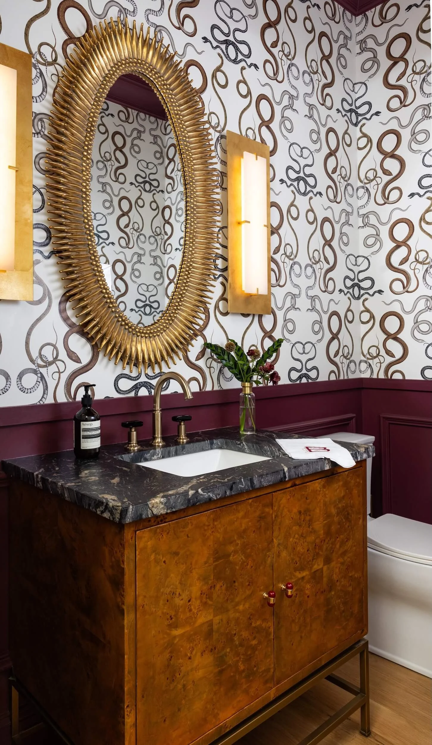 Bathroom vanity with gorgeous custom wallpaper, golden mirror, and oversized sconces