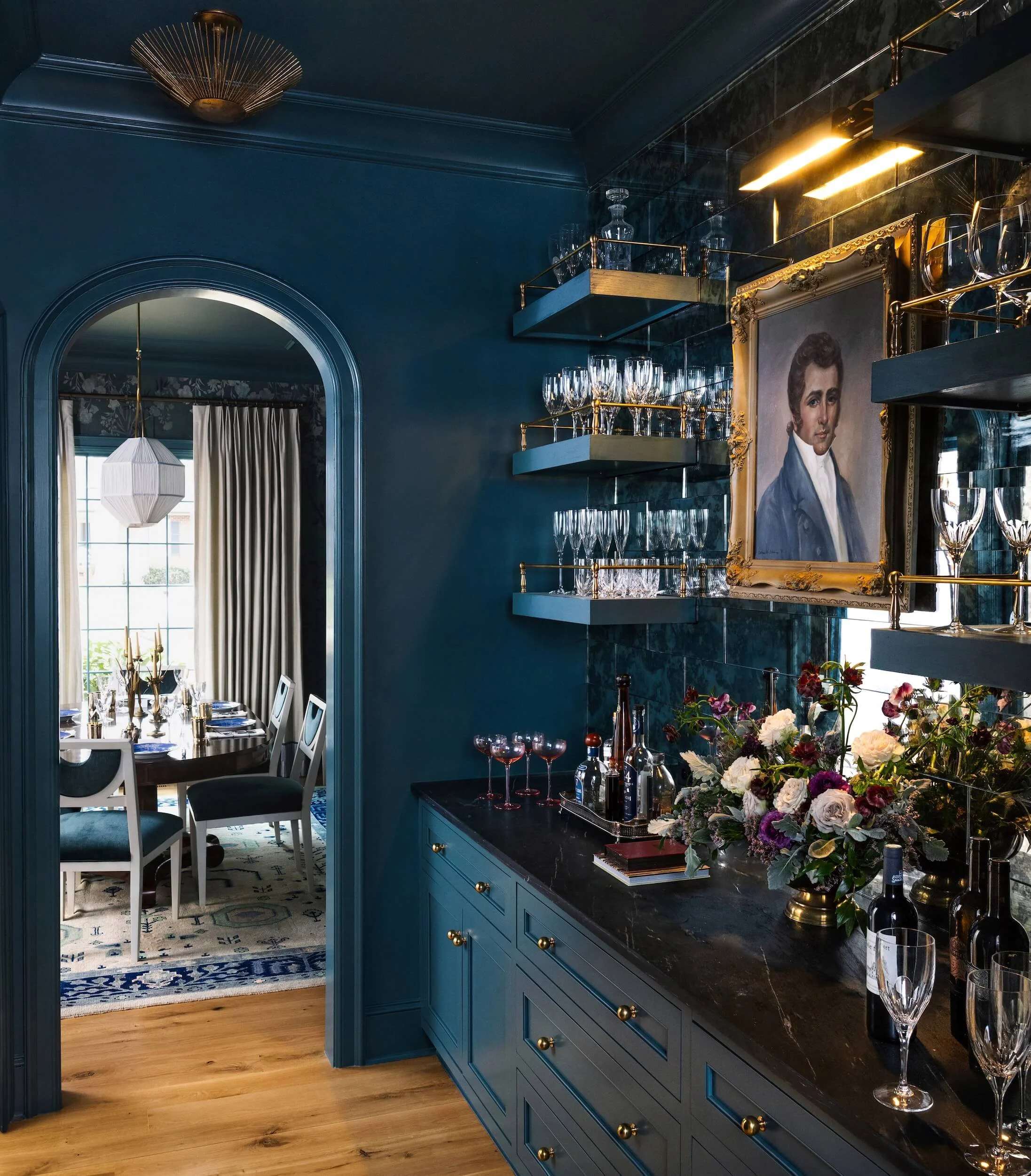 A peek at the butler's pantry, also color drenched in teal with a dark counter top, oil portrait, and covered in glassware