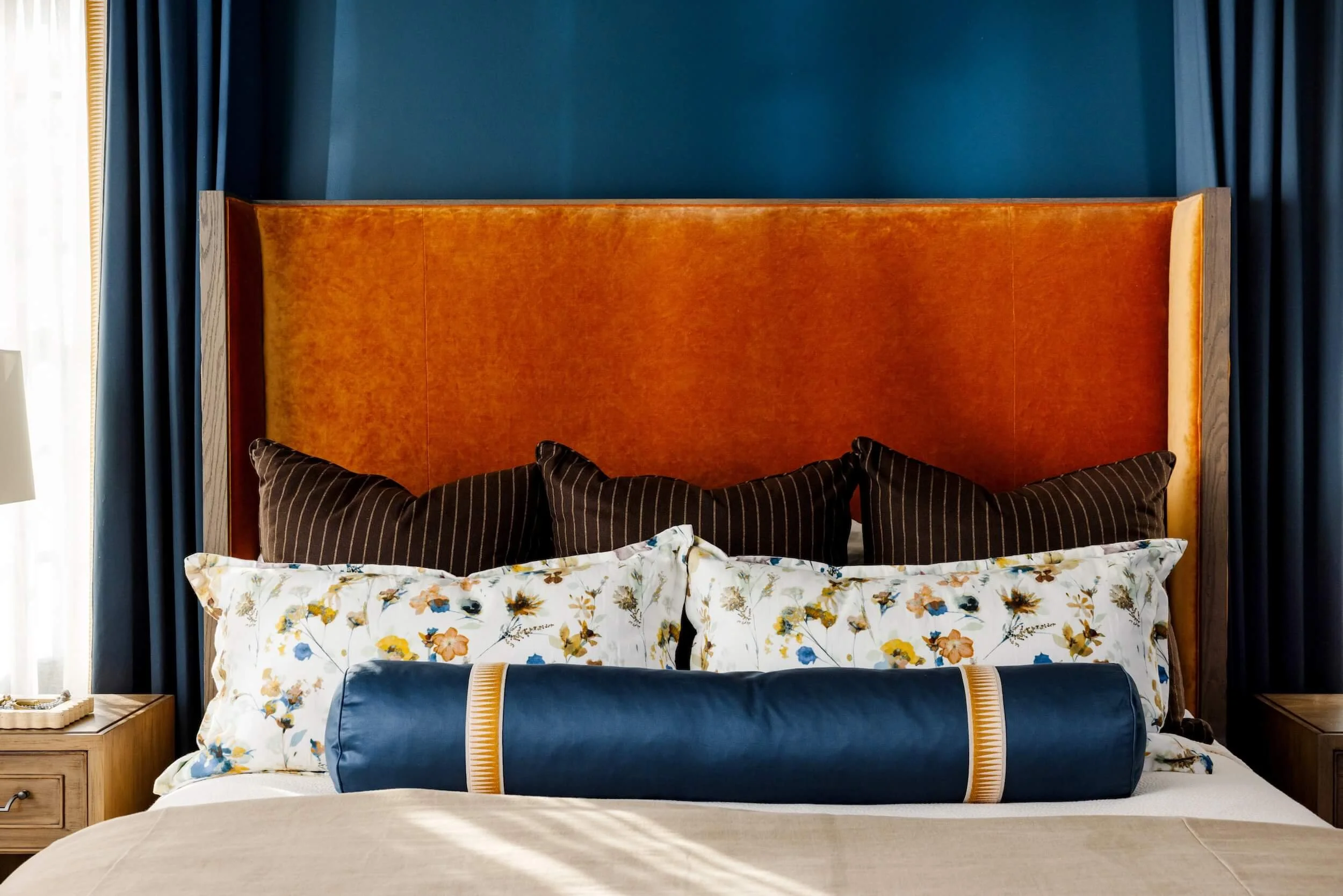 A close up of the velvet headboard, brown throw pillows, floral pillows, and blue satin bolster pillow 