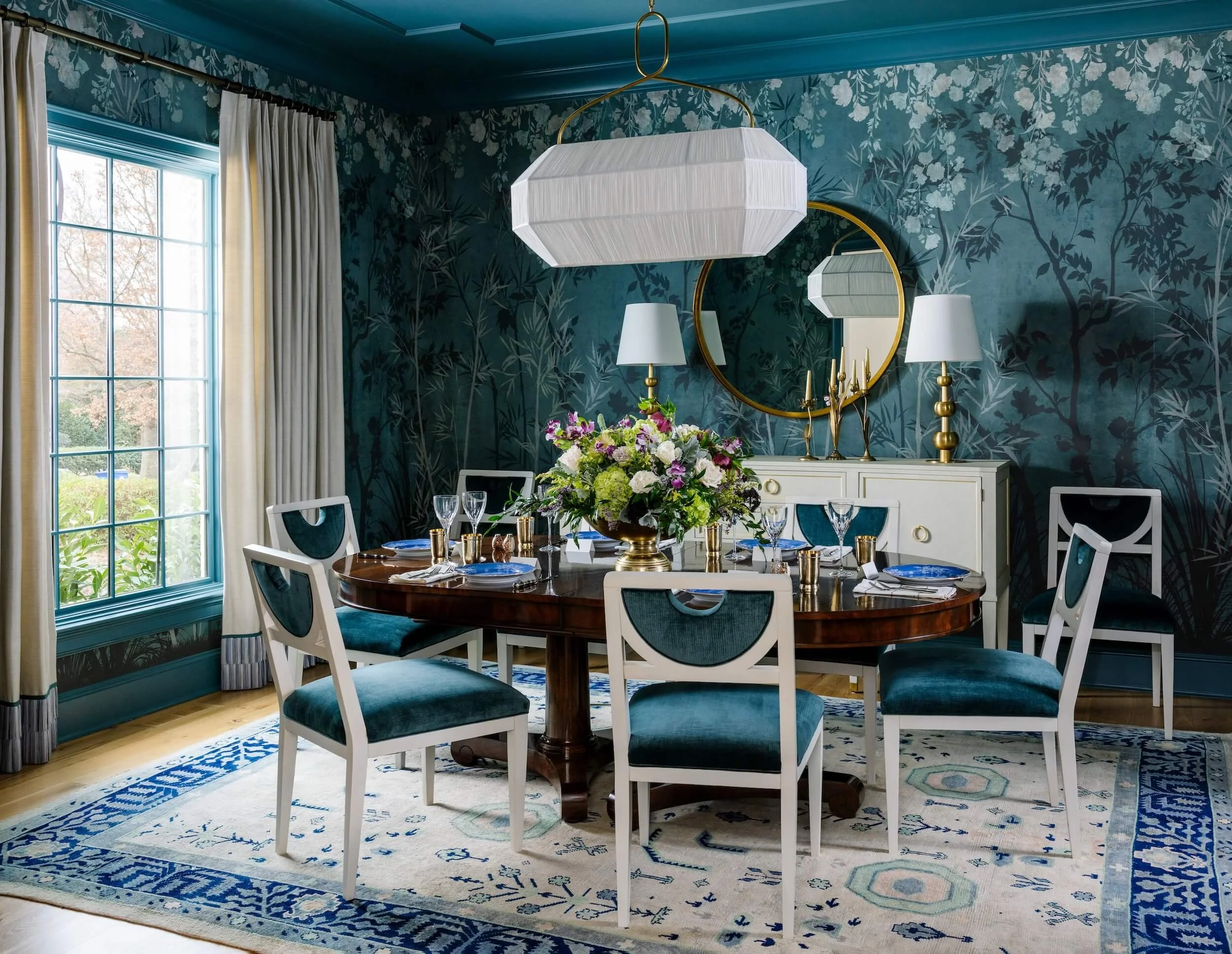 Teal dining room with floral wallpaper, velvet chairs, and beautiful blue rug