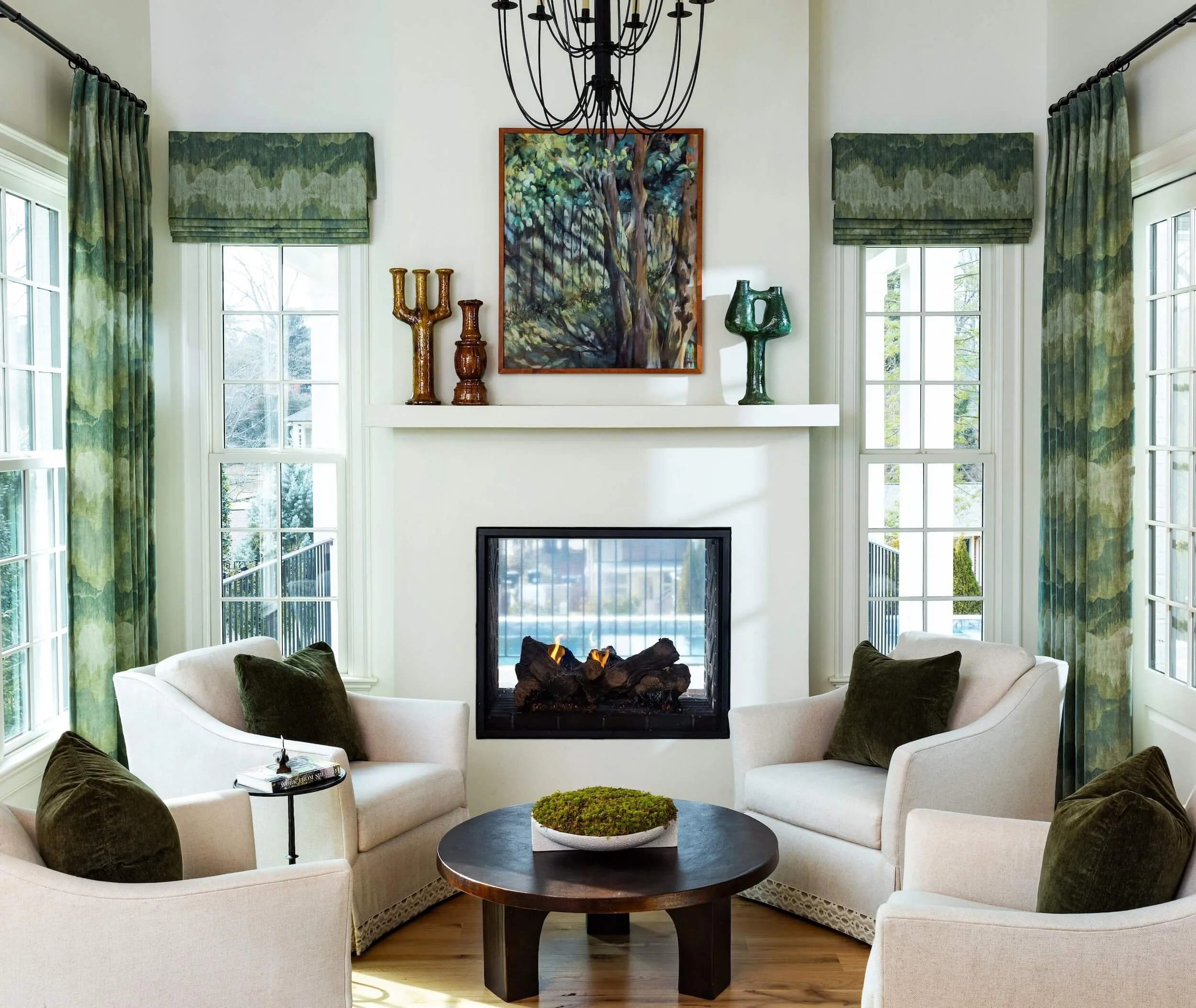 White sitting room with 4 chairs and a fireplace with green curtains and accents throughout 