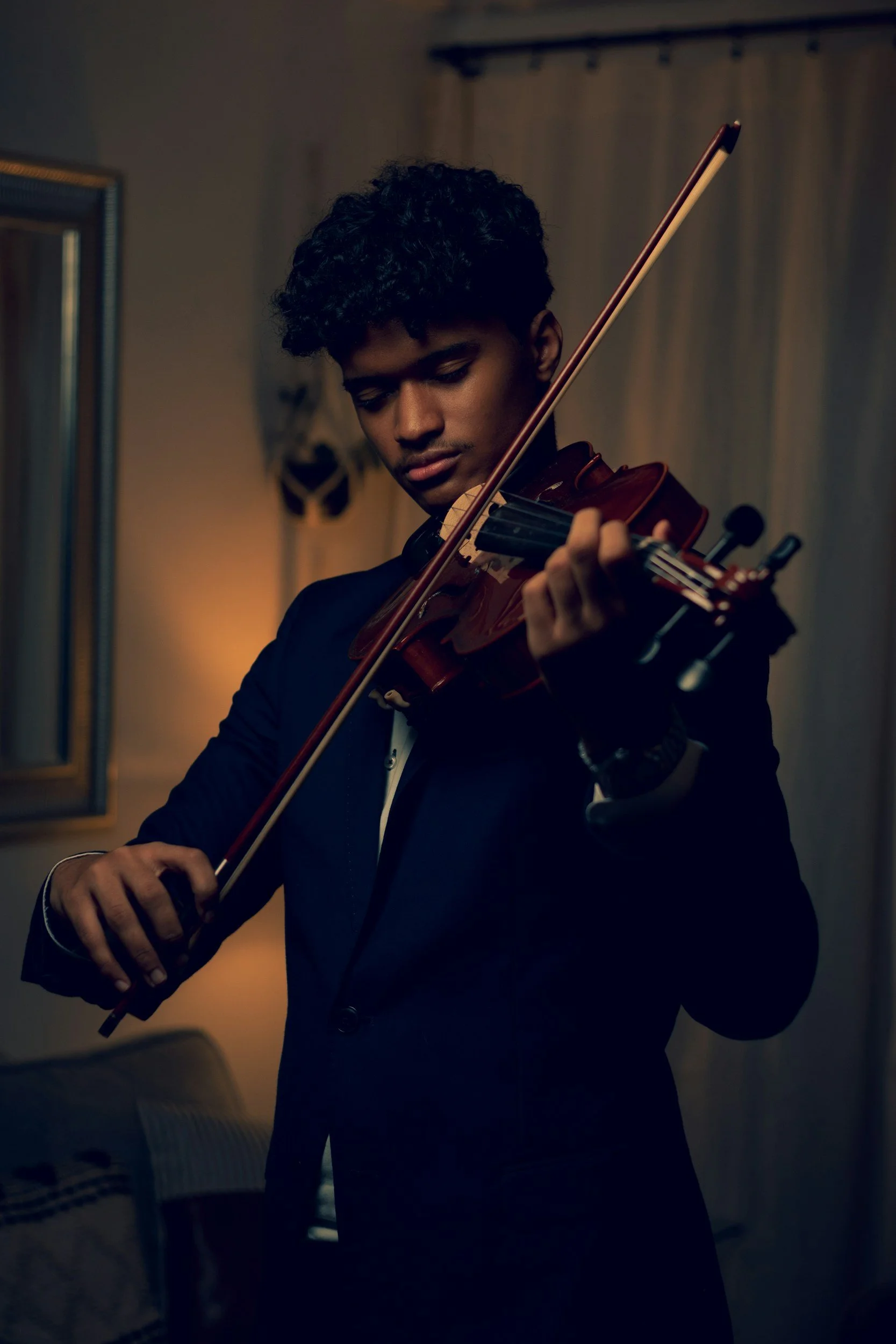 A young man playing a violin indoors, wearing a formal black suit, with a focused expression.
