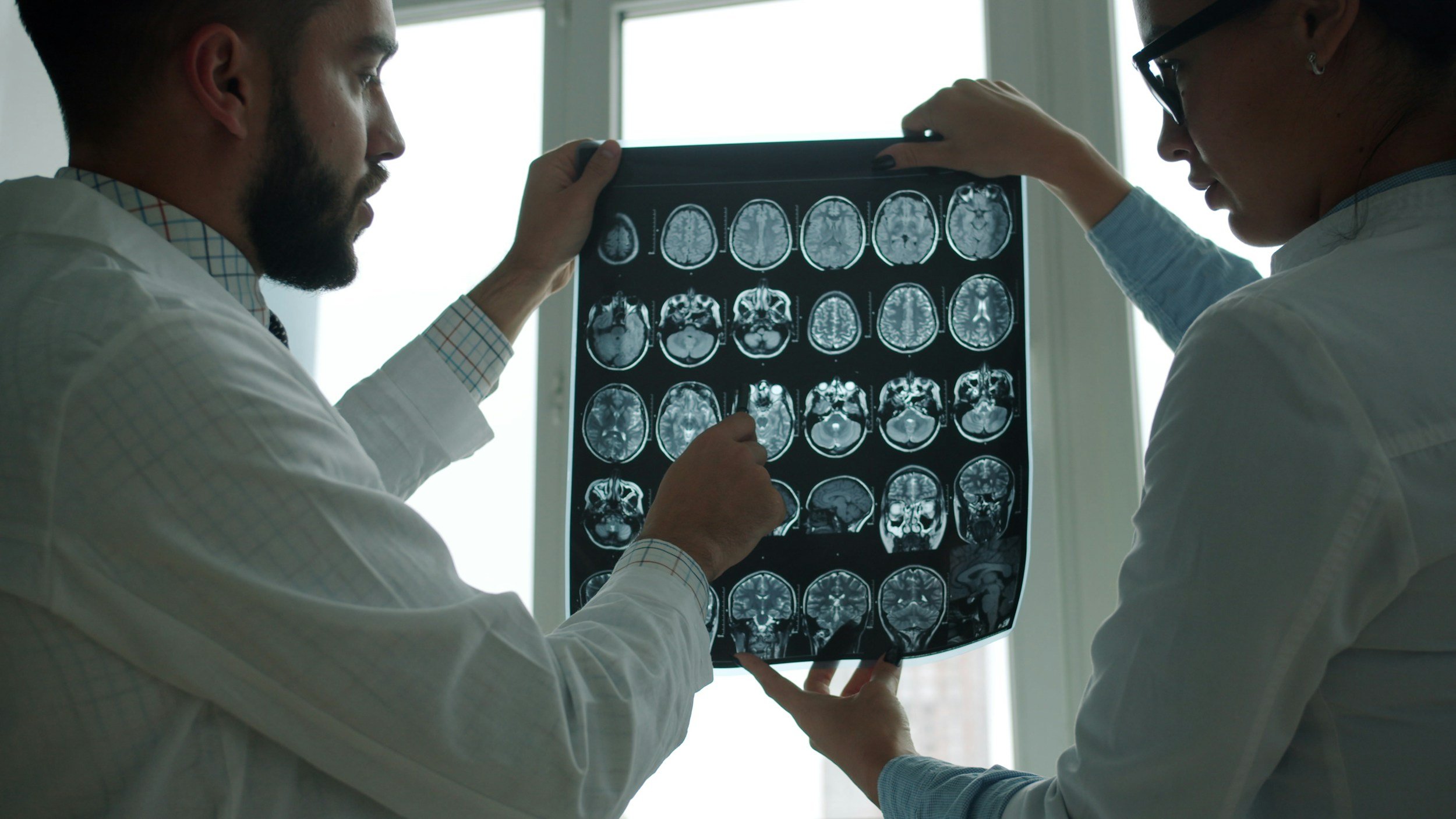 Two doctors examining a series of brain scan images on a lightbox in a medical office.