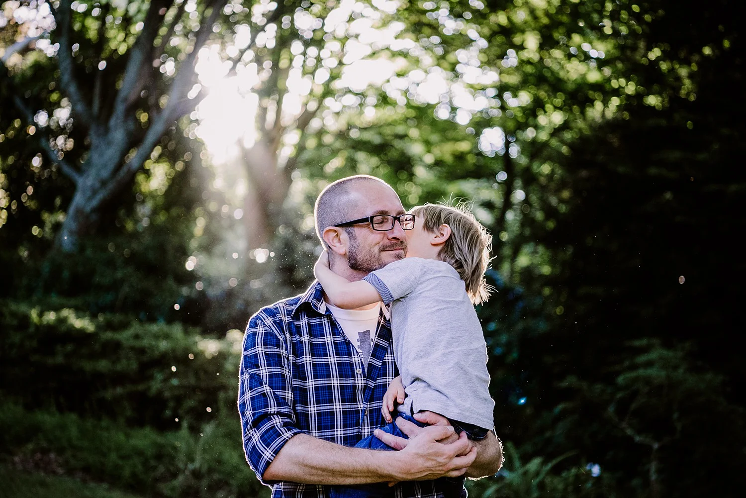 father cuddling son at sunset