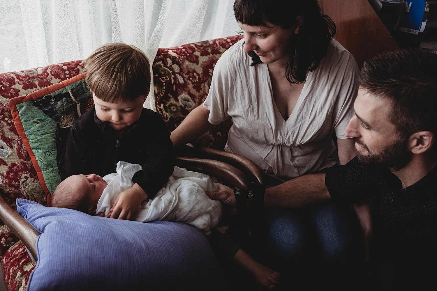 big brother holding newborn brother with parents 