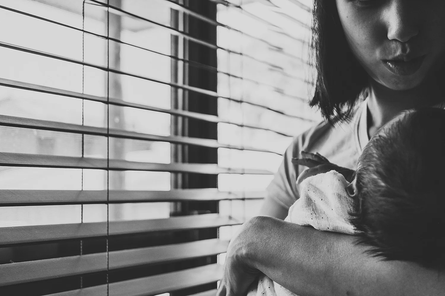 mother soothing baby near window