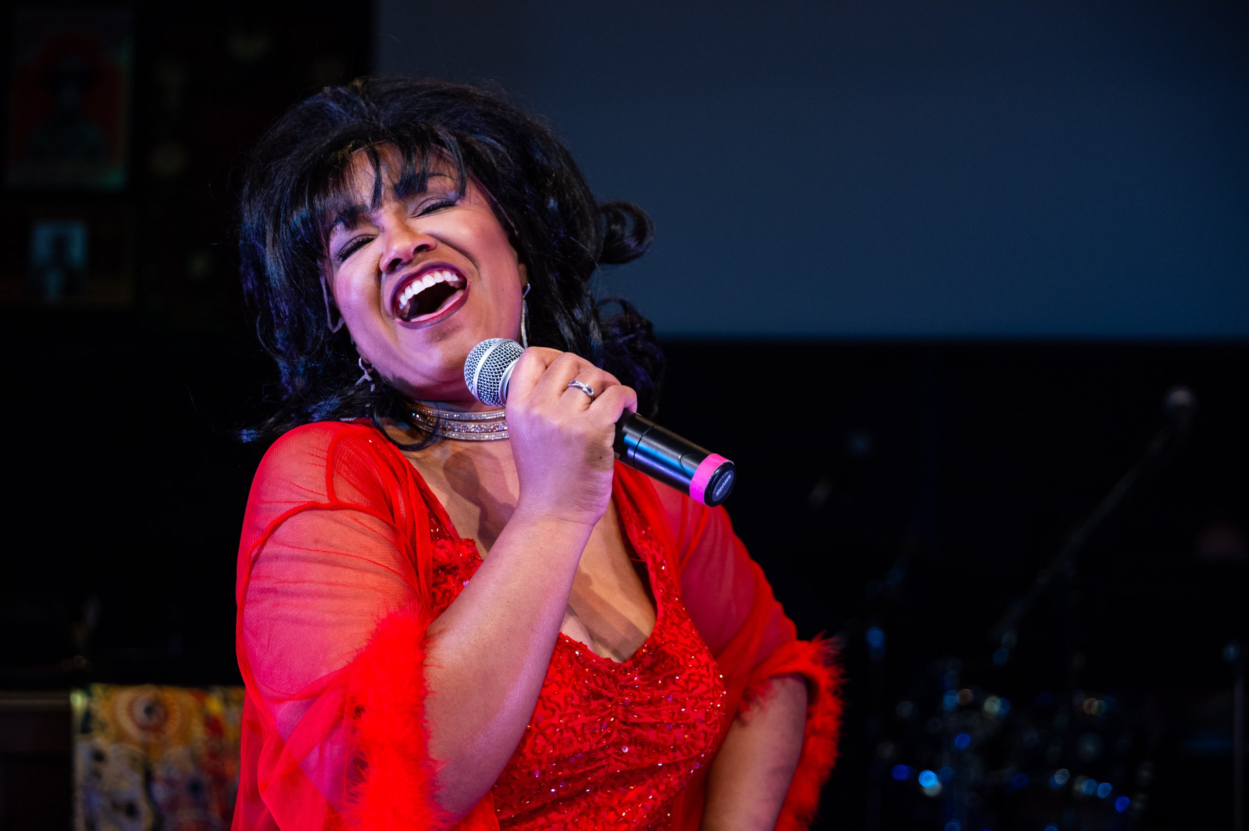 Safira in red dress singing as Aretha Franklin in A Night with Janis Joplin
