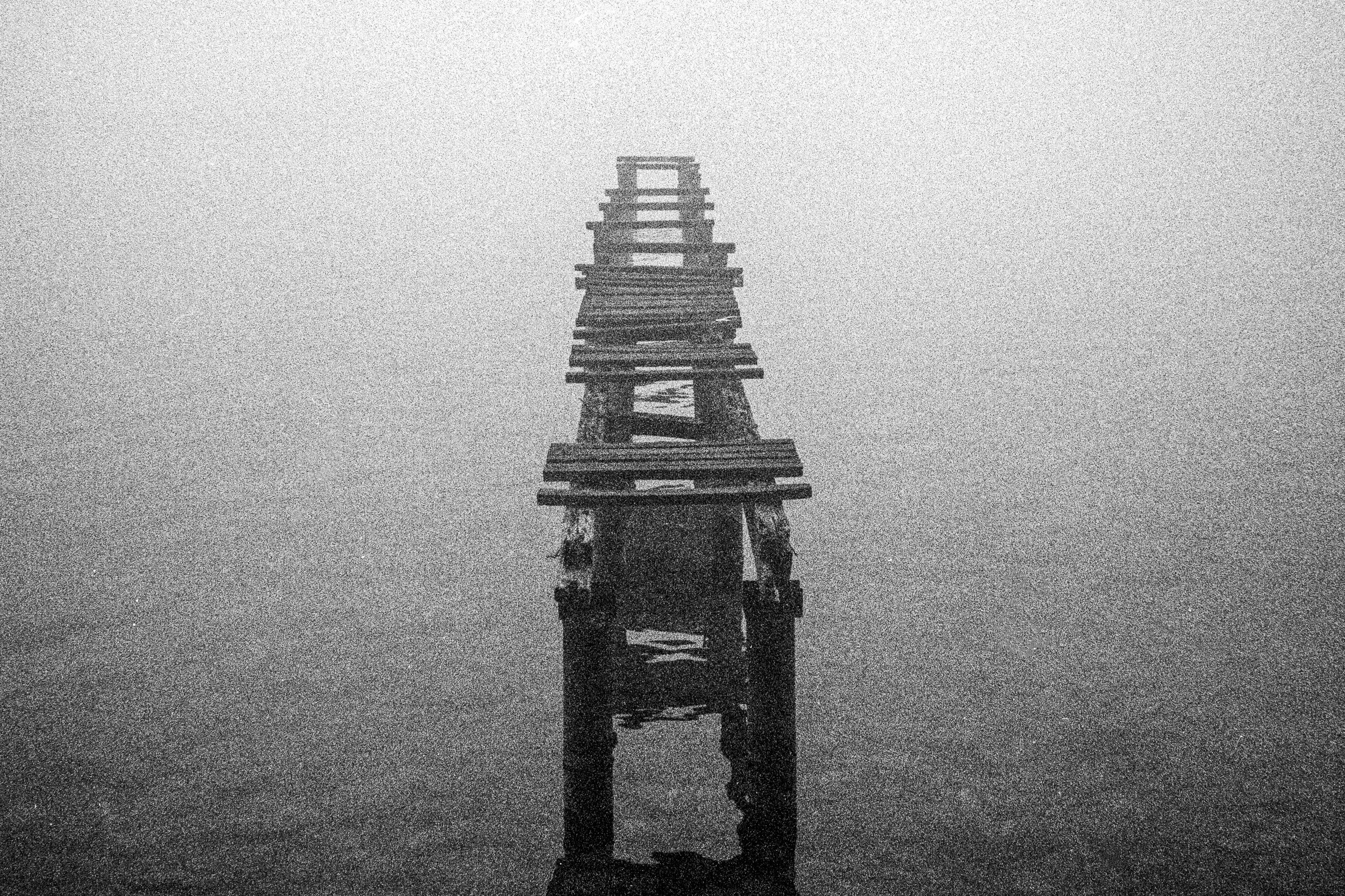 Black and white photo of an abandoned wooden pier extending into a foggy body of water.