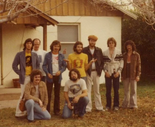 Jam session at Warren Jones' and Mark Lyons' house by the train tracks west of ASU in Tempe. Back row L to R: Zeke Gutierrez (guitar), Keith Miles (drums), Ted Goddard (guitar), Bob Fernandez (percussion), Jon Lane (bass), Joe Woznicki (guitar), Mike Hoenig (trombone); kneeling: Stan Sorensen (guitar), Warren Jones (bass). Photo by Allan Chase.