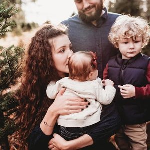 A woman holding a young child while a man and an older boy stand nearby outdoors.