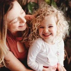 A woman and a young girl laughing and smiling together outdoors.