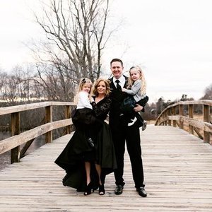 A family posing on a wooden bridge outdoors in winter, with trees in the background.