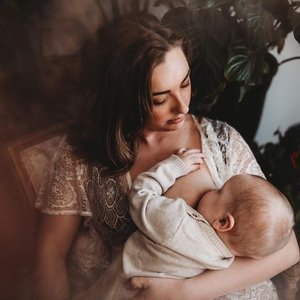 A woman holding and breastfeeding a baby in a cozy, indoor setting.