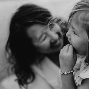 A woman and a young girl sharing a joyful moment, with the girl touching the woman's face.