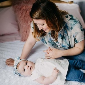 Woman smiling and gently touching a baby lying on a bed