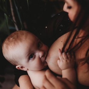 Baby breastfeeding from mother in a dimly lit setting.