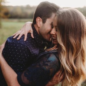 A couple sharing an affectionate embrace outdoors during daytime, smiling with faces close together.
