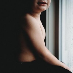 A woman sitting by a window, with her back and shoulder visible in the image.