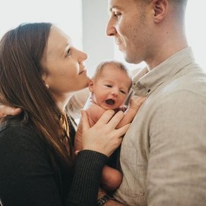 A woman and a man holding a crying baby between them, looking at each other indoors.
