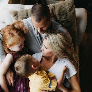 Family of four sitting closely, smiling and embracing on a couch.