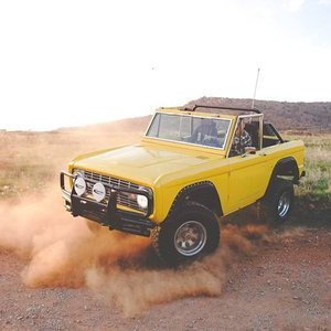Yellow vintage off-road vehicle kicking up dust in a desert landscape.