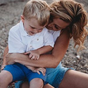 A woman and a young boy sitting outdoors, smiling and enjoying each other's company.