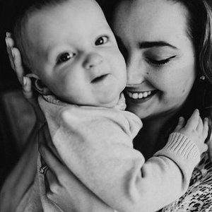 A woman smiling and holding a baby close in a black and white photo.