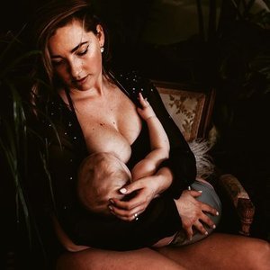 A woman breastfeeding a baby while sitting in a dimly lit room.