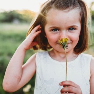 Young girl outdoors holding a yellow dandelion flower in front of her nose.