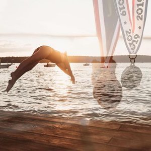 Person performing a backflip near the water at sunset, with medals hanging nearby.