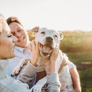 Two women and a smiling dog outdoors at sunset.