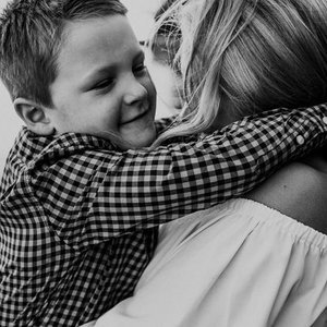 A young boy hugging an adult woman, smiling with his eyes closed.